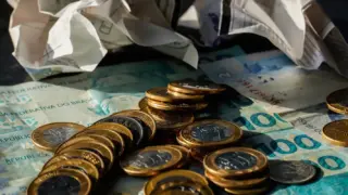 Moedas e cédulas de real sobre a mesa, ilustrando a alta do dólar e a queda do Ibovespa após a eleição
