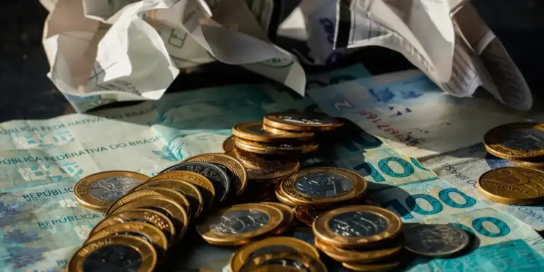 Moedas e cédulas de real sobre a mesa, ilustrando a alta do dólar e a queda do Ibovespa após a eleição