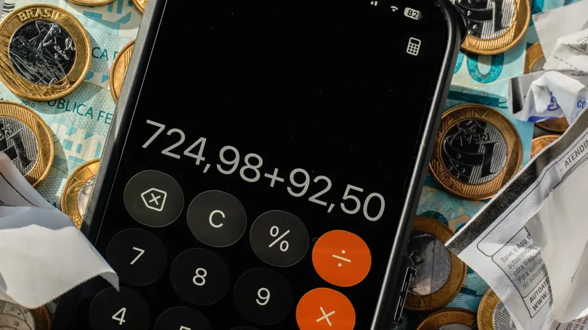 Calculadora de celular sobre moedas de real e notas fiscais amassadas, ilustrando nanoempreendedor e MEI