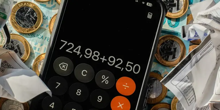 Calculadora de celular sobre moedas de real e notas fiscais amassadas, ilustrando nanoempreendedor e MEI